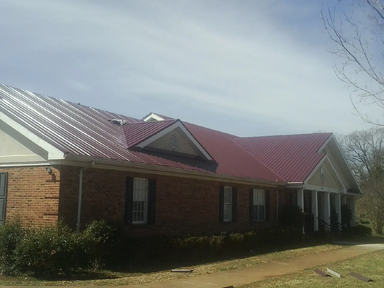 Red metal roof with gabled entries on a long brick building, from a Hail Damage Roof Repair job in Bellville
